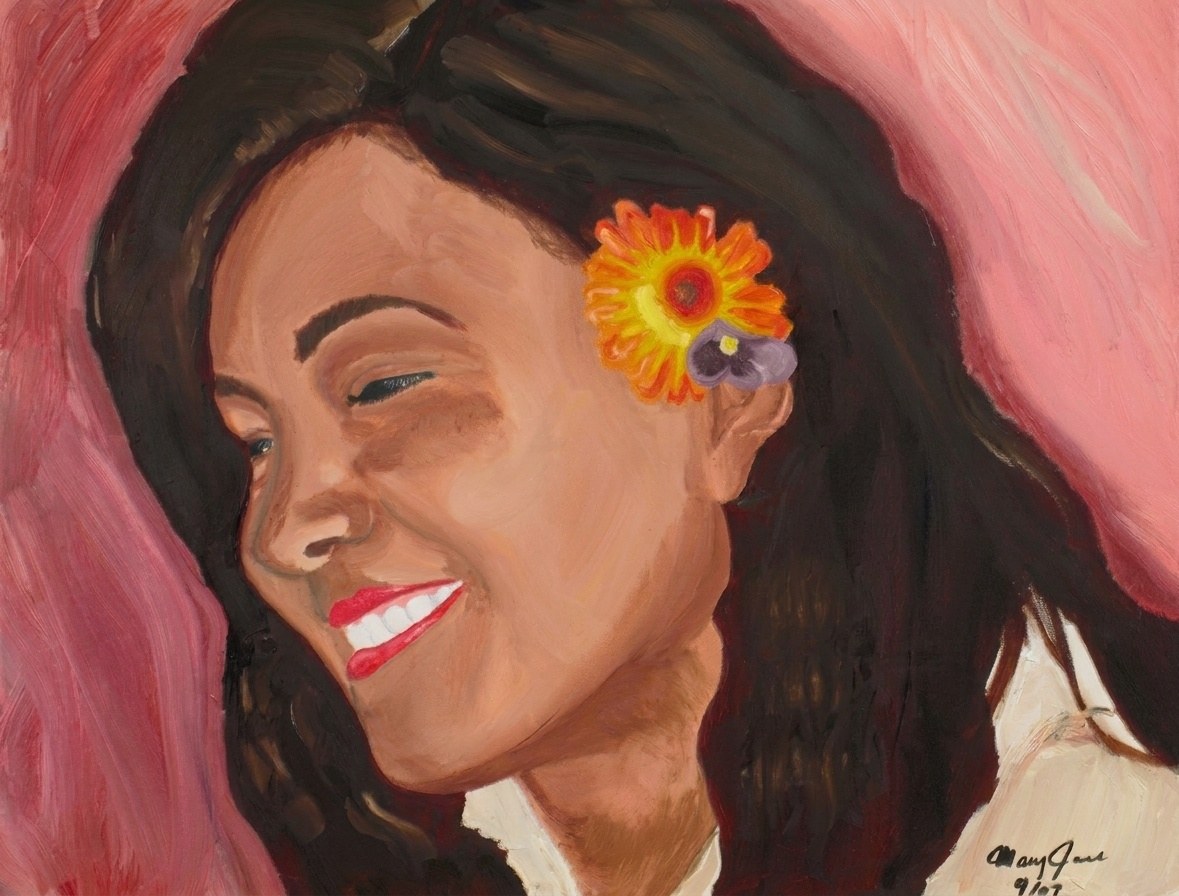 A woman with long dark hair smiles with her eyes closed, head tilted, an orange flower and a small purple one tucked behind her ear, against a pink ground